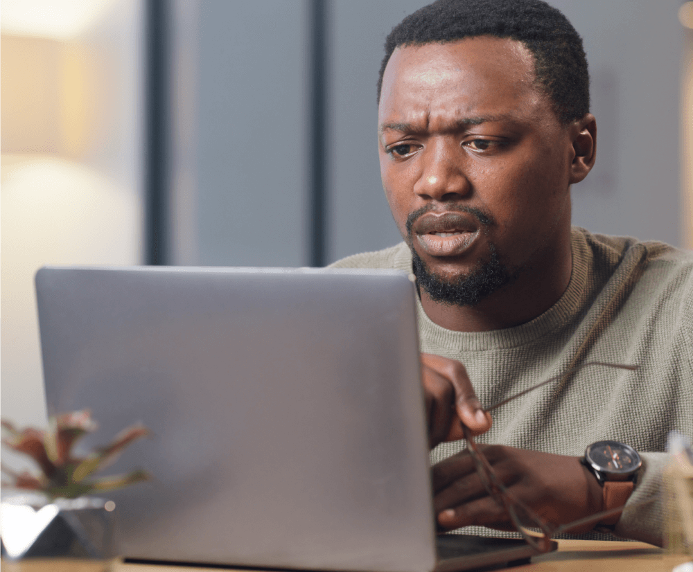 A man sits at a table, focused on his laptop, engaged in work or research.