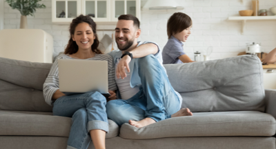 Couple on couch looking at a laptop with children running